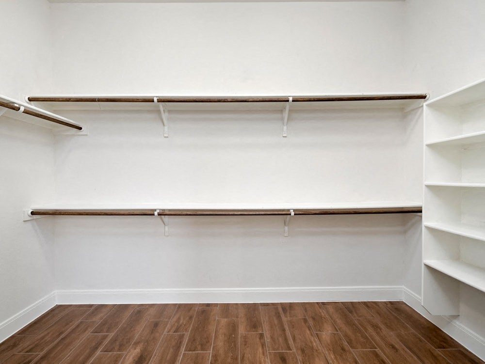 a walk in closet with white walls and shelves and a wood floor