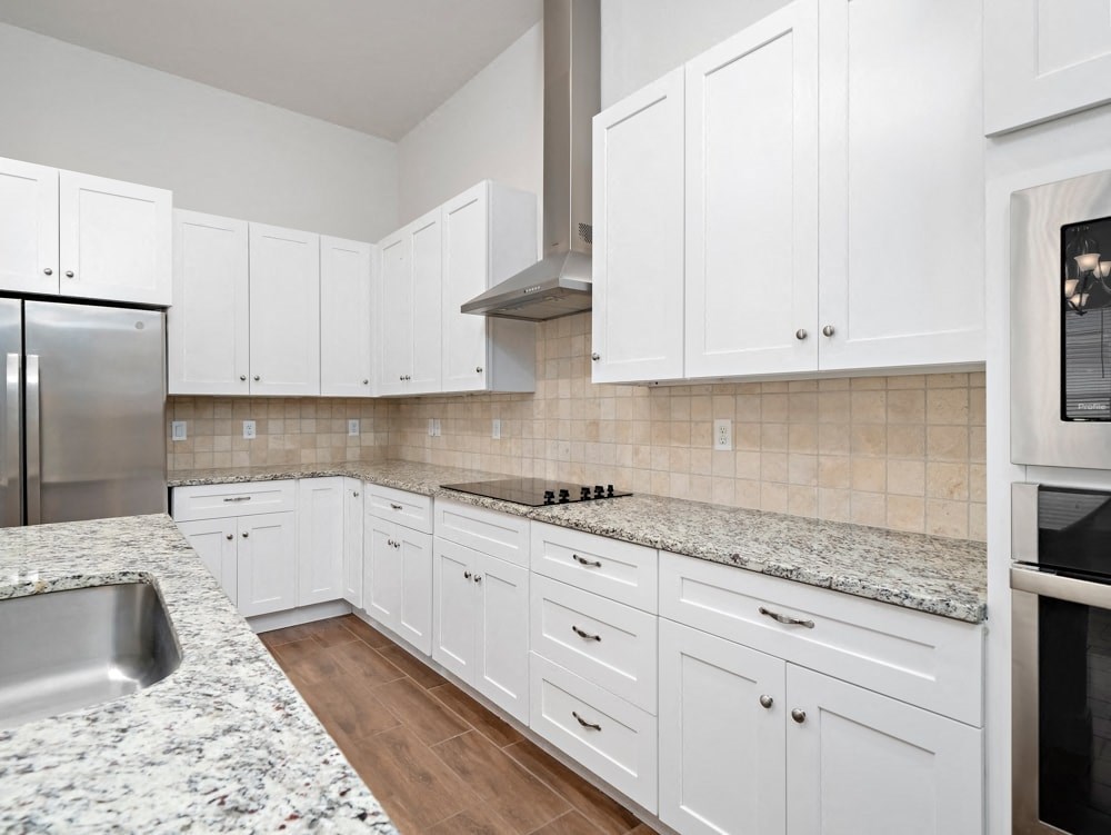 a kitchen with white cabinets and marble counter tops