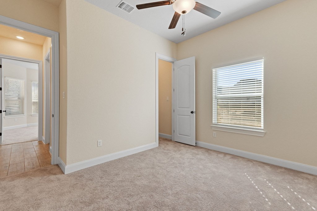 an empty living room with a ceiling fan and a door to a hallway