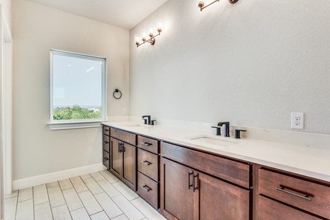 a bathroom with two sinks and wooden cabinets and a window