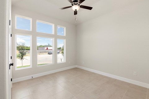 an empty living room with a ceiling fan and large windows