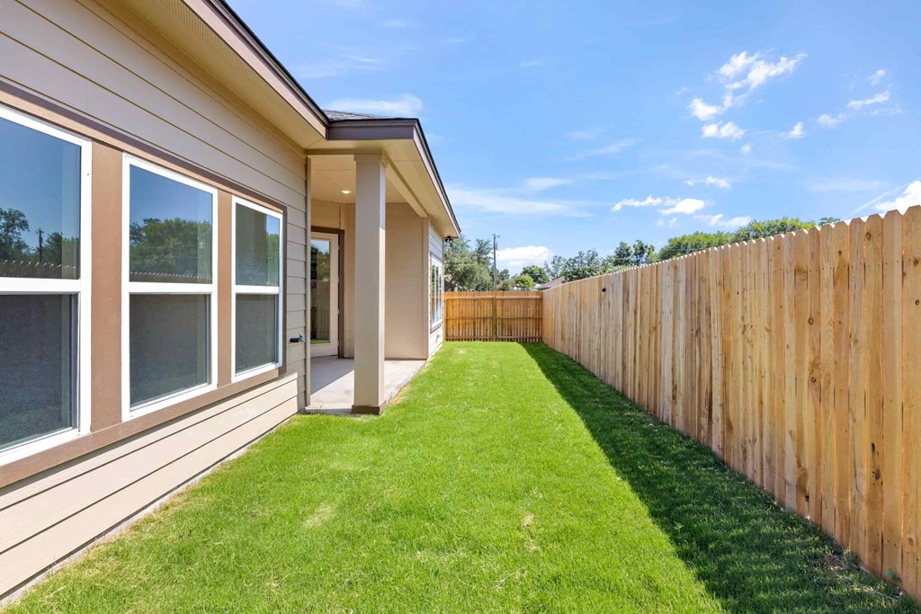 a yard with a wooden fence and a lawn next to a house