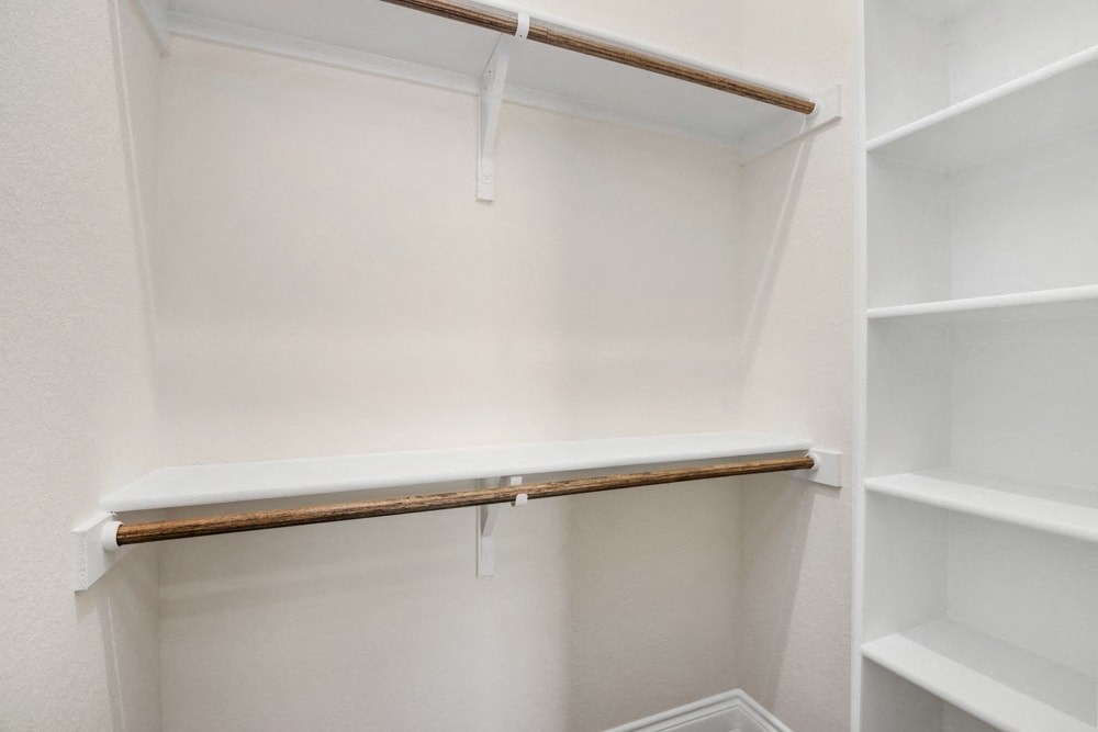 a walk in closet with white shelves and a wooden shelf