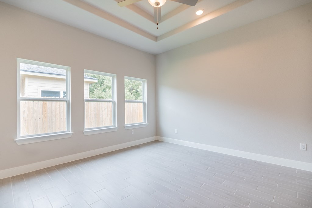 an empty living room with a ceiling fan and three windows