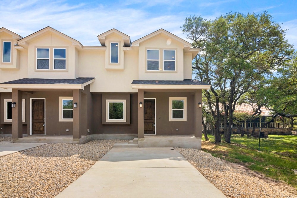 a beige and brown house with a driveway and trees