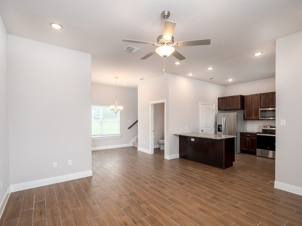 an empty living room with a ceiling fan and a kitchen