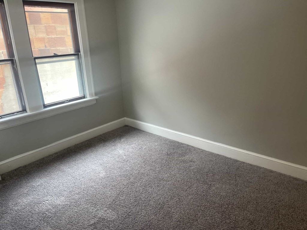 A room with a grey carpet and a window.