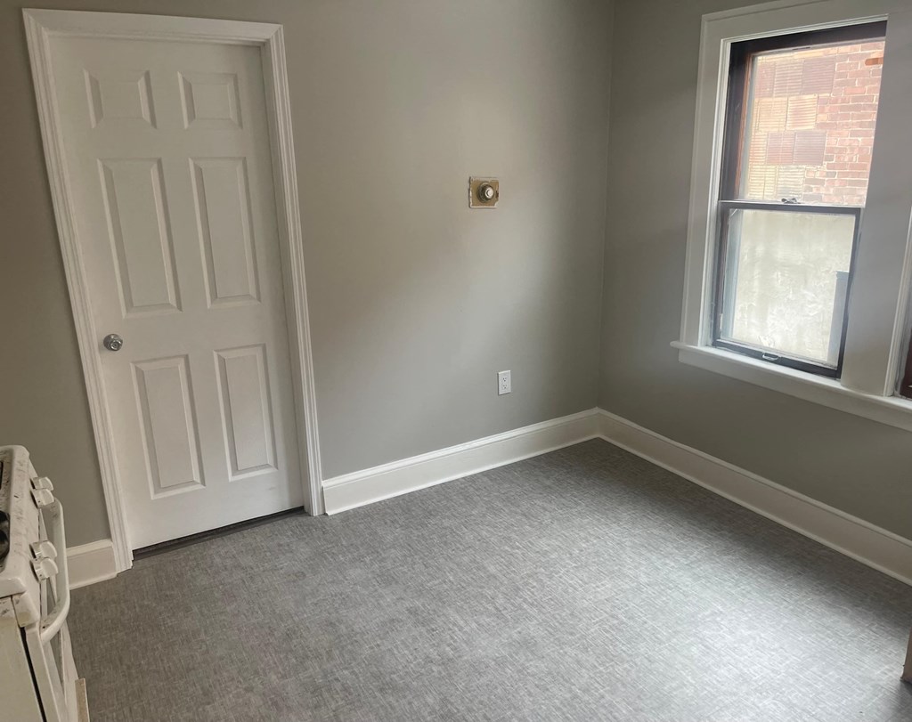 A room with a white door, grey carpet, and a window.