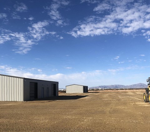 two buildings in the middle of a dirt field with a blue sky