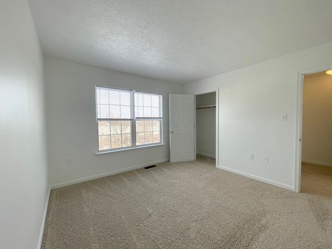the living room of an apartment with carpet and a window