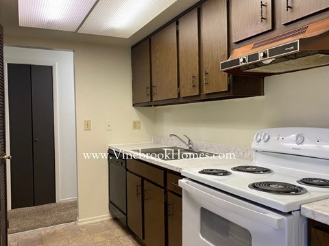 A kitchen with a white stove top oven and wooden cabinets.
