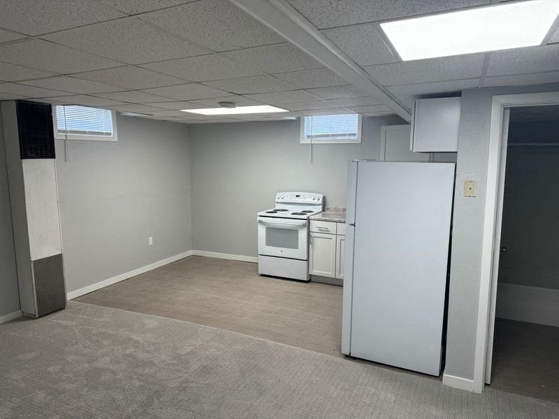 A kitchen area with a refrigerator, oven, and microwave in a room with carpeted floor.