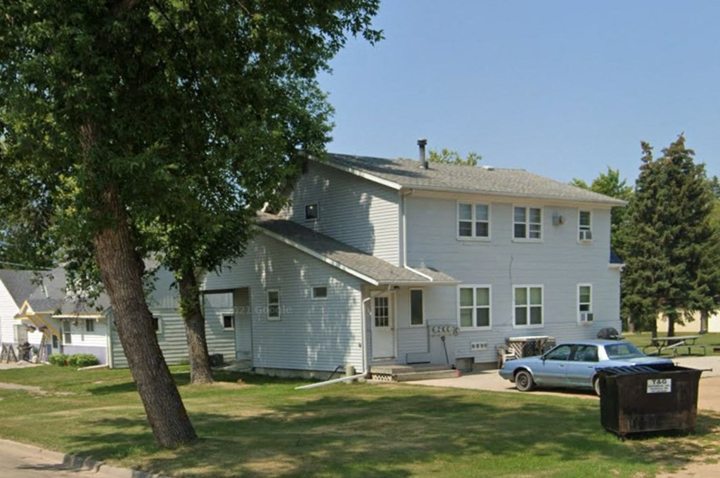 A white house with a blue car parked in front.