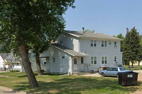 A white house with a blue car parked in front.