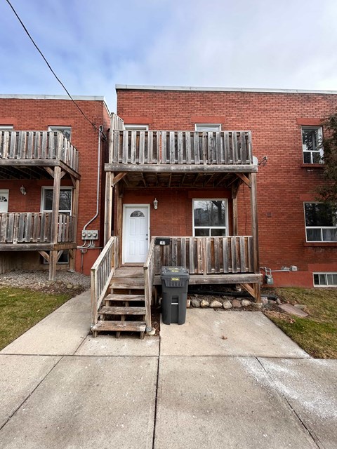 the front of a brick house with a wooden porch and a trash can