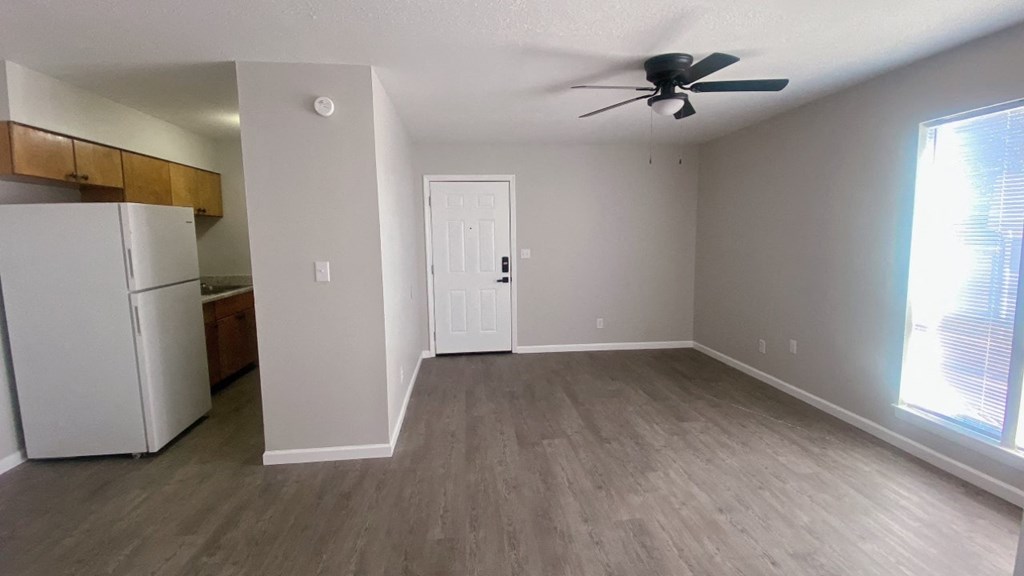 an empty living room with a refrigerator and a ceiling fan