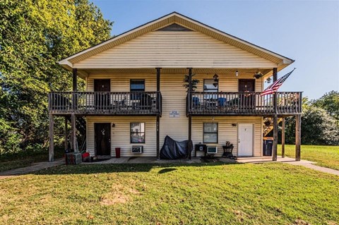 the front of a yellow house with a flag on the balcony