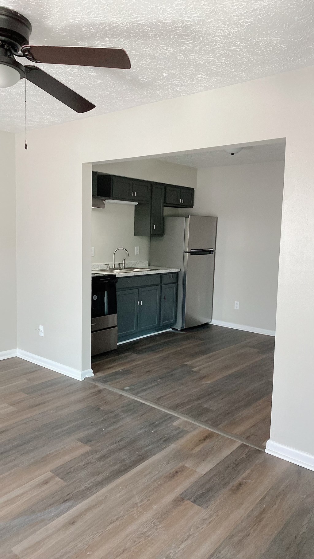 an empty living room with a kitchen and a ceiling fan