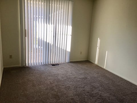 a living room with carpet and a large window with vertical blinds