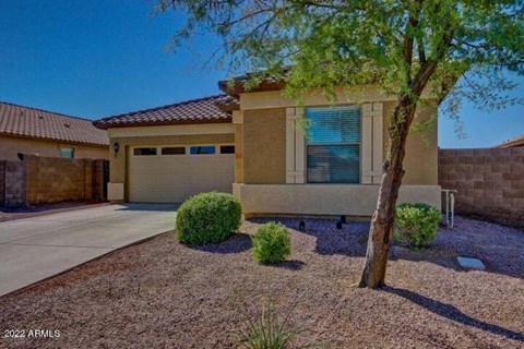 A house with a brown roof and tan walls has a tree in front of it.
