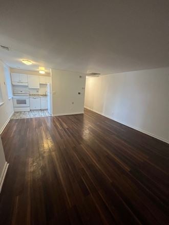 an empty living room with wooden floors and a kitchen