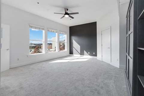 A spacious room with a ceiling fan and large windows overlooking a residential area.