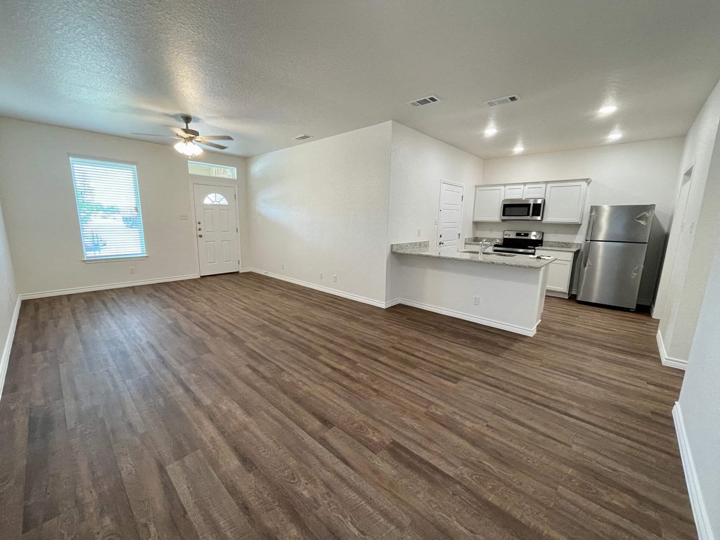 an empty living room with a kitchen and a ceiling fan