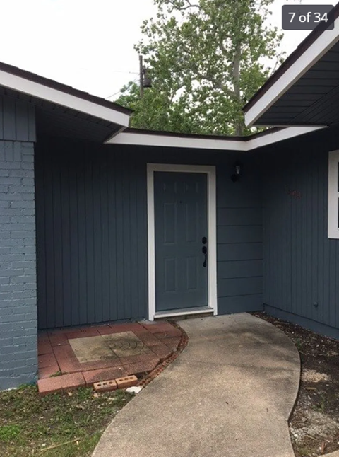 A blue house with a white door and a concrete walkway.
