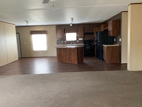 an empty living room with a kitchen with black appliances