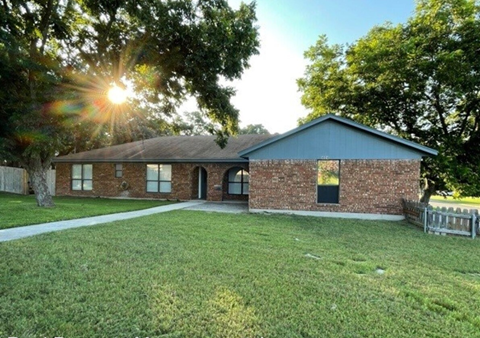the front of a brick house with a yard and the sun shining behind it
