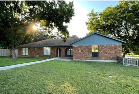 the front of a brick house with a grassy yard and trees