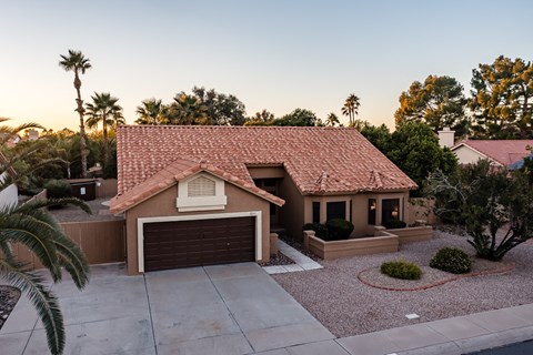 A house with a brown roof and a brown garage door is surrounded by palm trees.