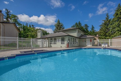 A swimming pool in front of a house with a deck and a fence.