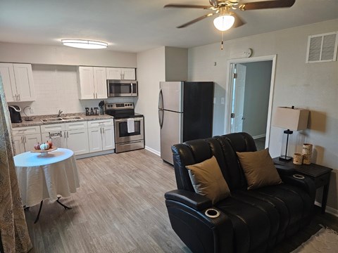 A black leather couch with two pillows sits in a living room with a kitchen in the background.