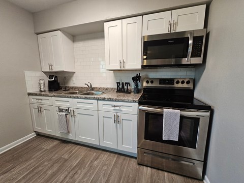 A kitchen with white cabinets and a black microwave above the stove.