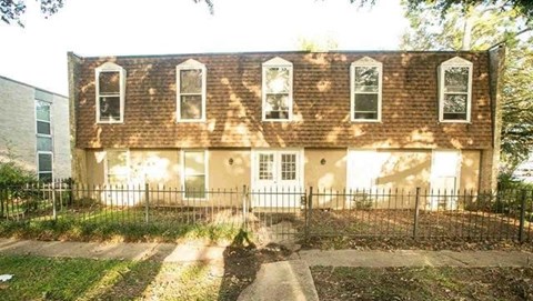 A brown building with white trim and windows is surrounded by a black fence.