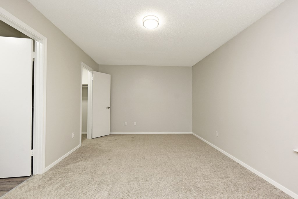 an empty room with white walls and carpet and a door to a closet