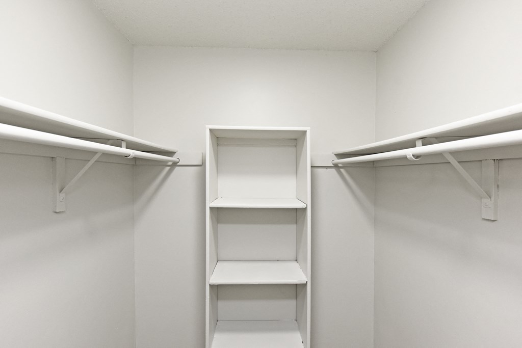 a walk in closet with white shelves and a shelving unit in it