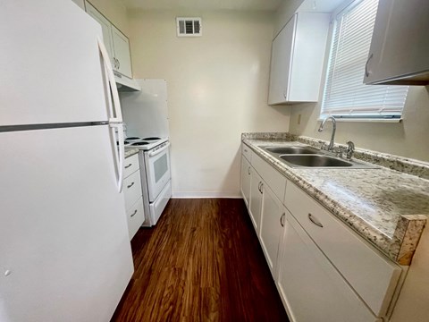 A kitchen with a white fridge, sink and cabinets.