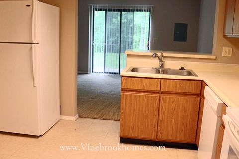 A white refrigerator is in a kitchen with a sink and wooden cabinets.