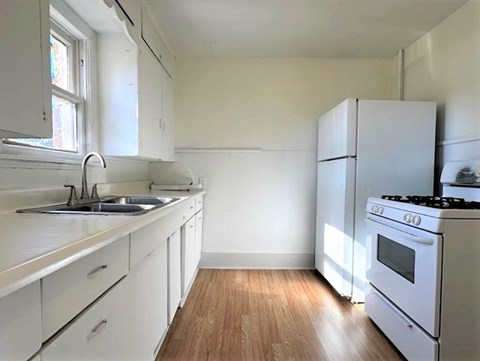 A white kitchen with wooden floors and white appliances.