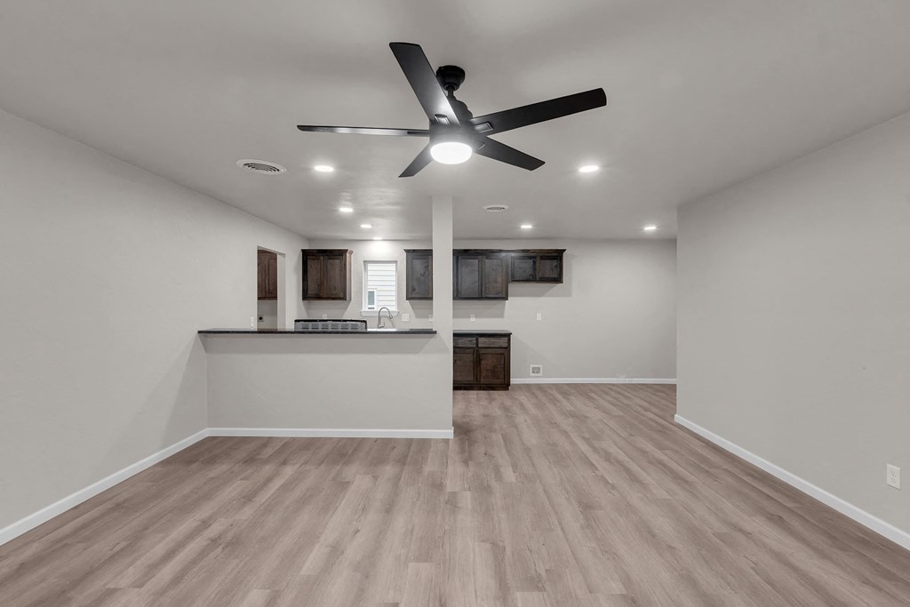 an empty living room with a ceiling fan and a kitchen