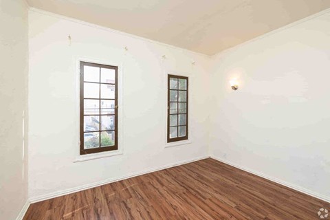 A room with two windows and wooden floors.