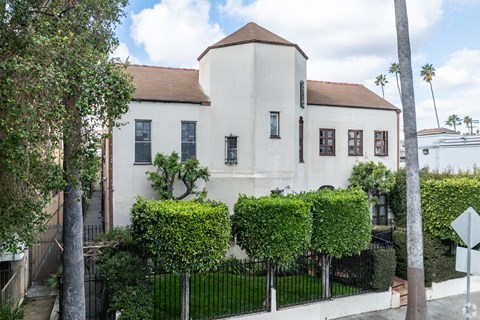 A white building with a brown roof and a black fence in front of it.