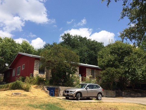 A silver car is parked in front of a red house.