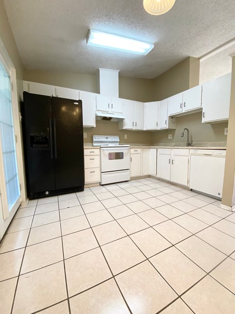 A kitchen with a black refrigerator, white cabinets, and a white oven.