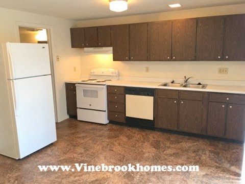 A white refrigerator stands in a kitchen with brown cabinets and white countertops.