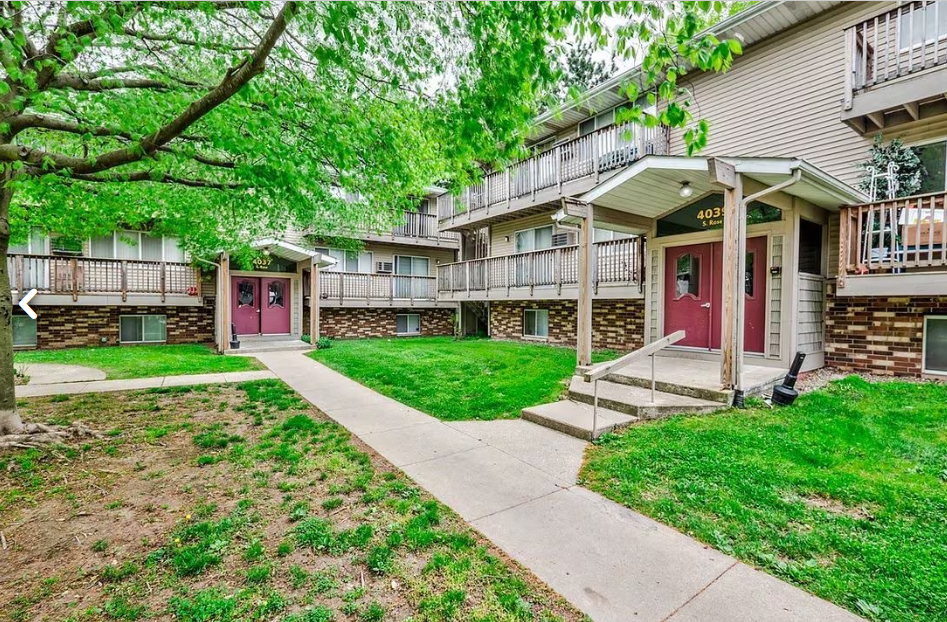 the outlook of an apartment building with a sidewalk and grass