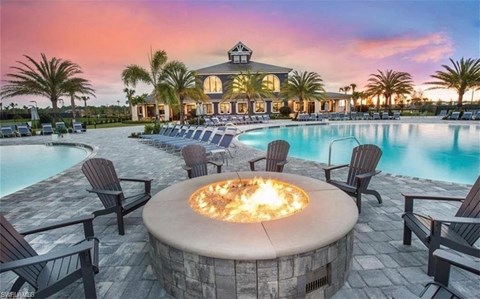 a fire pit in front of a swimming pool with a hotel in the background