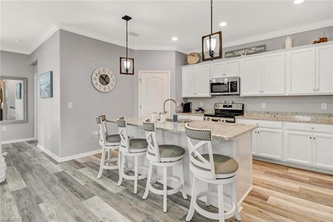 a kitchen with white cabinets and a bar with three chairs